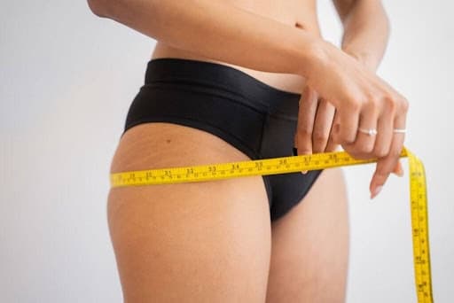 Woman measuring her thigh with a yellow tape measure for skin tightening treatment.