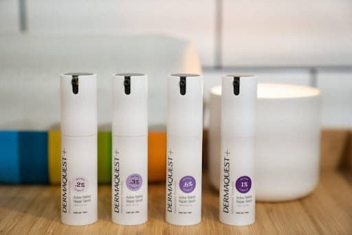 Four Dermalux LED light therapy serums on a wooden surface in a clinic setting.