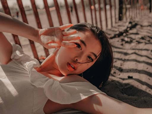 Woman enjoying a sunny day at the beach, relaxing on sand with a playful peace sign gesture.