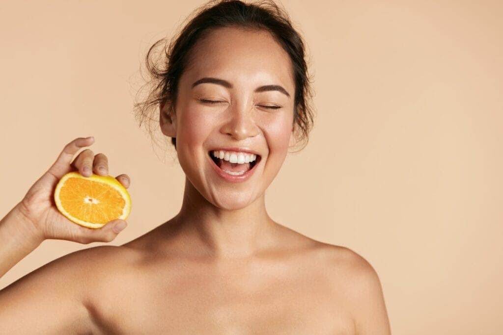 Happy woman holding a fresh orange, promoting skincare and natural beauty at Cannelle Skin Clinic.