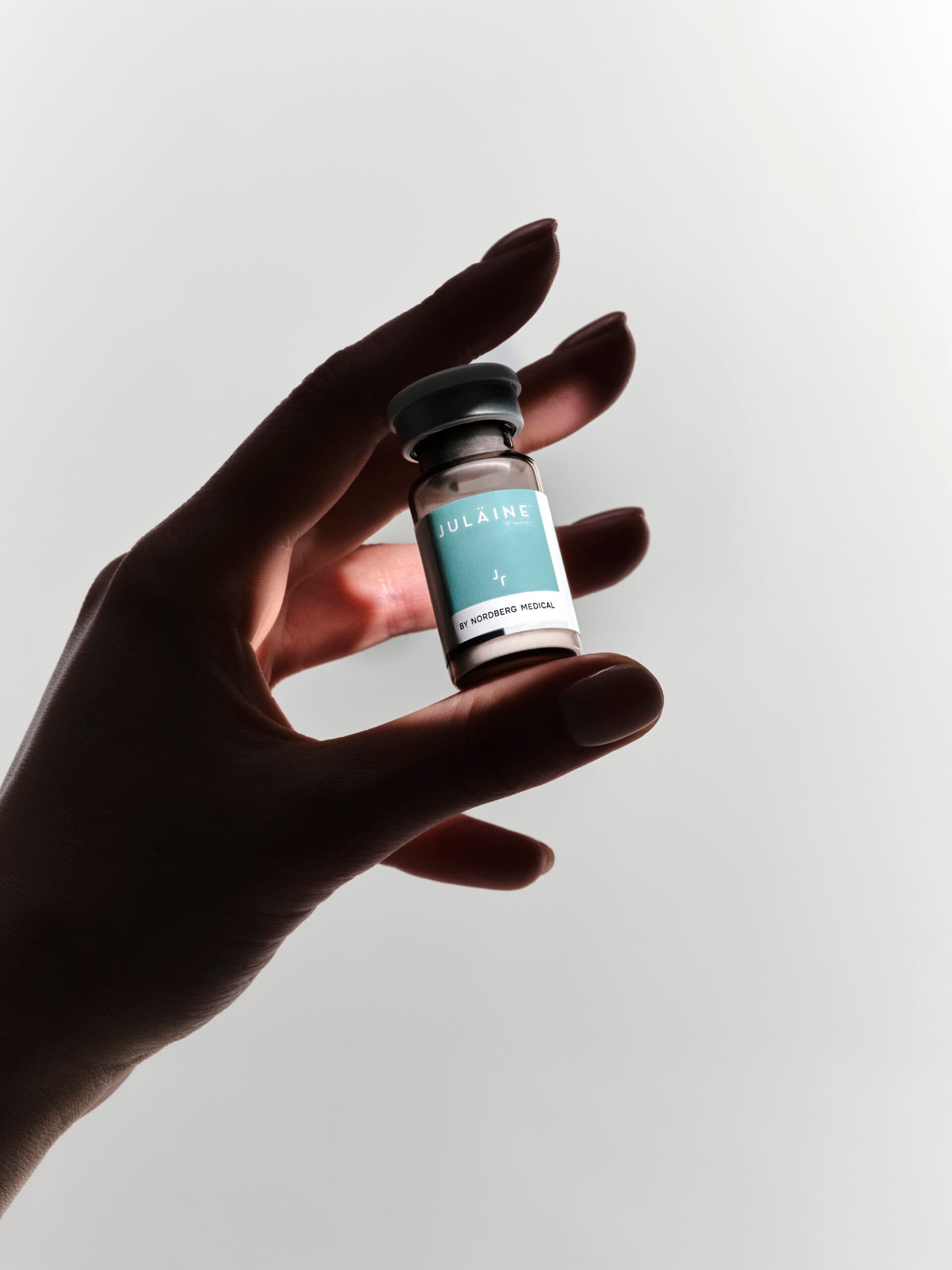 Hand holding a small vial of Vulaine injectable treatment against a plain background.